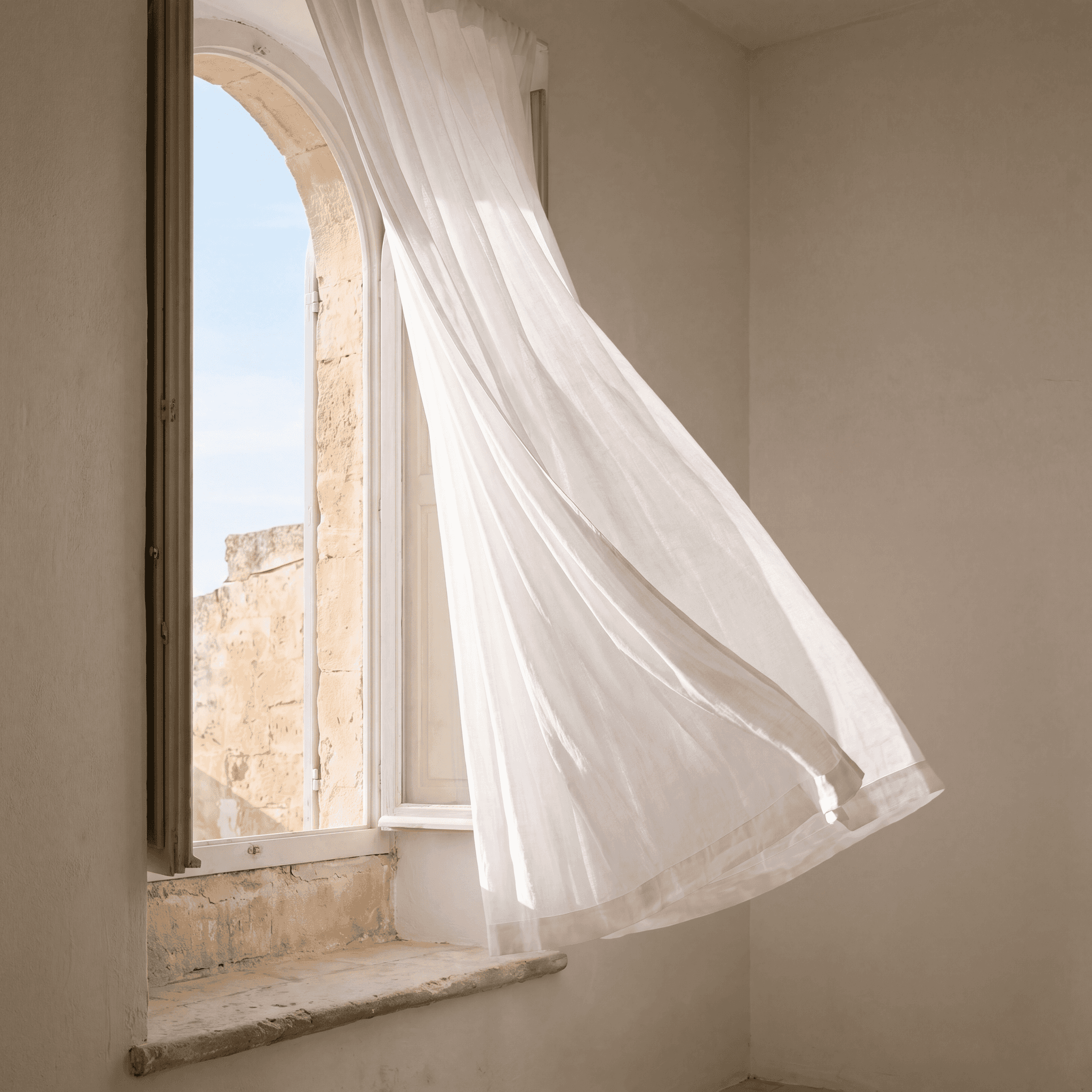 White linen curtain billowing through an open Mediterranean window