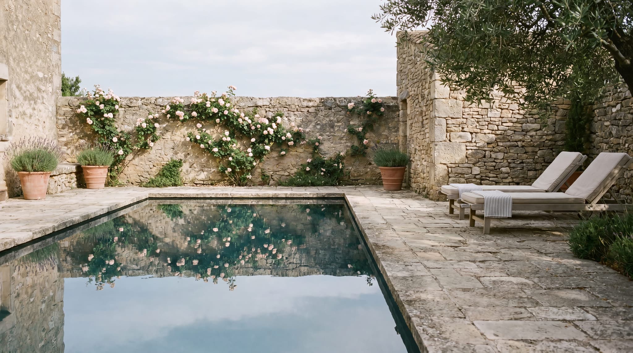 Boutique hotel pool at late afternoon, stone surround, still water reflecting the sky